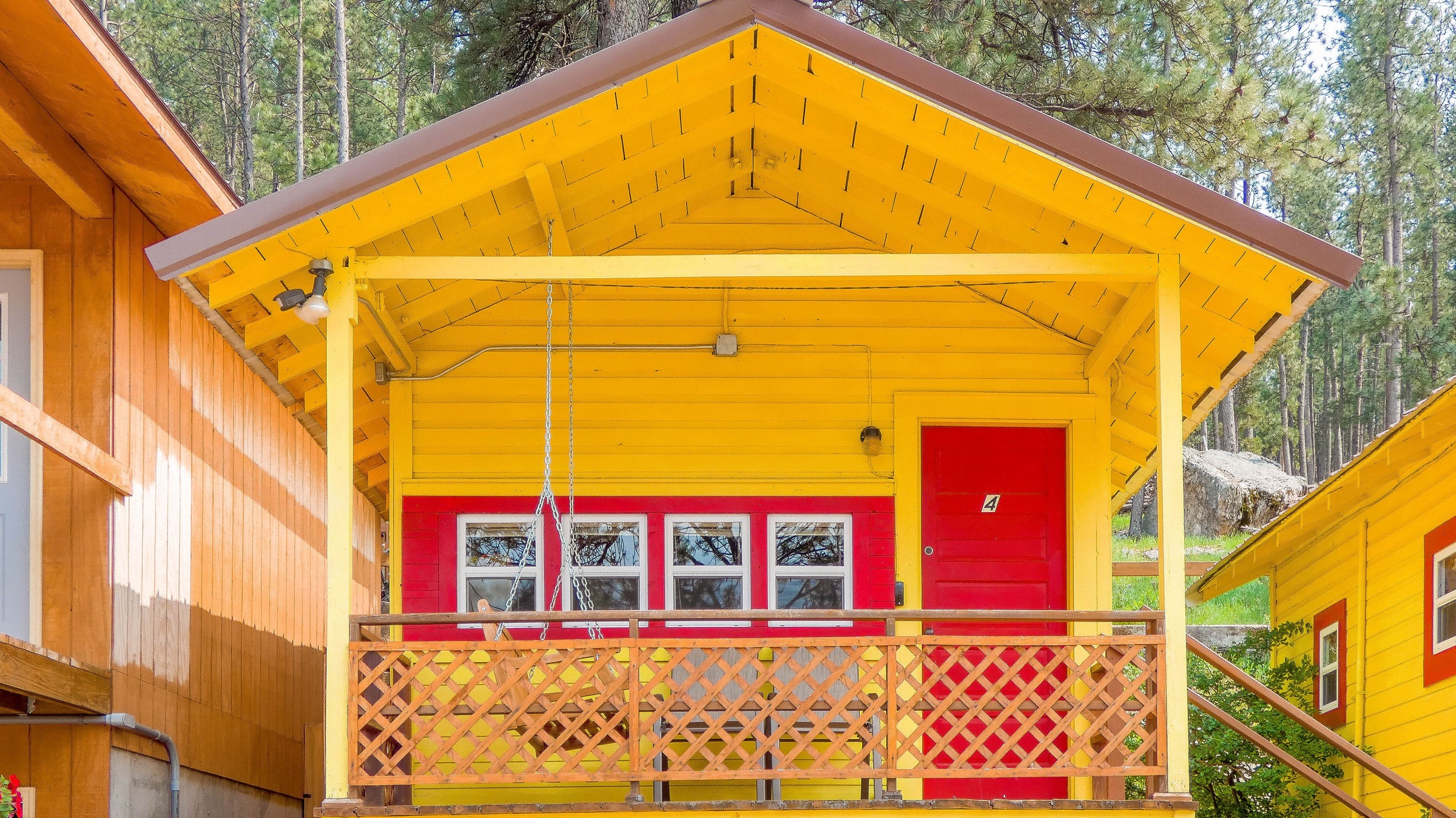 Cabin 4: bright yellow porch with red door and windows and a lattice rail