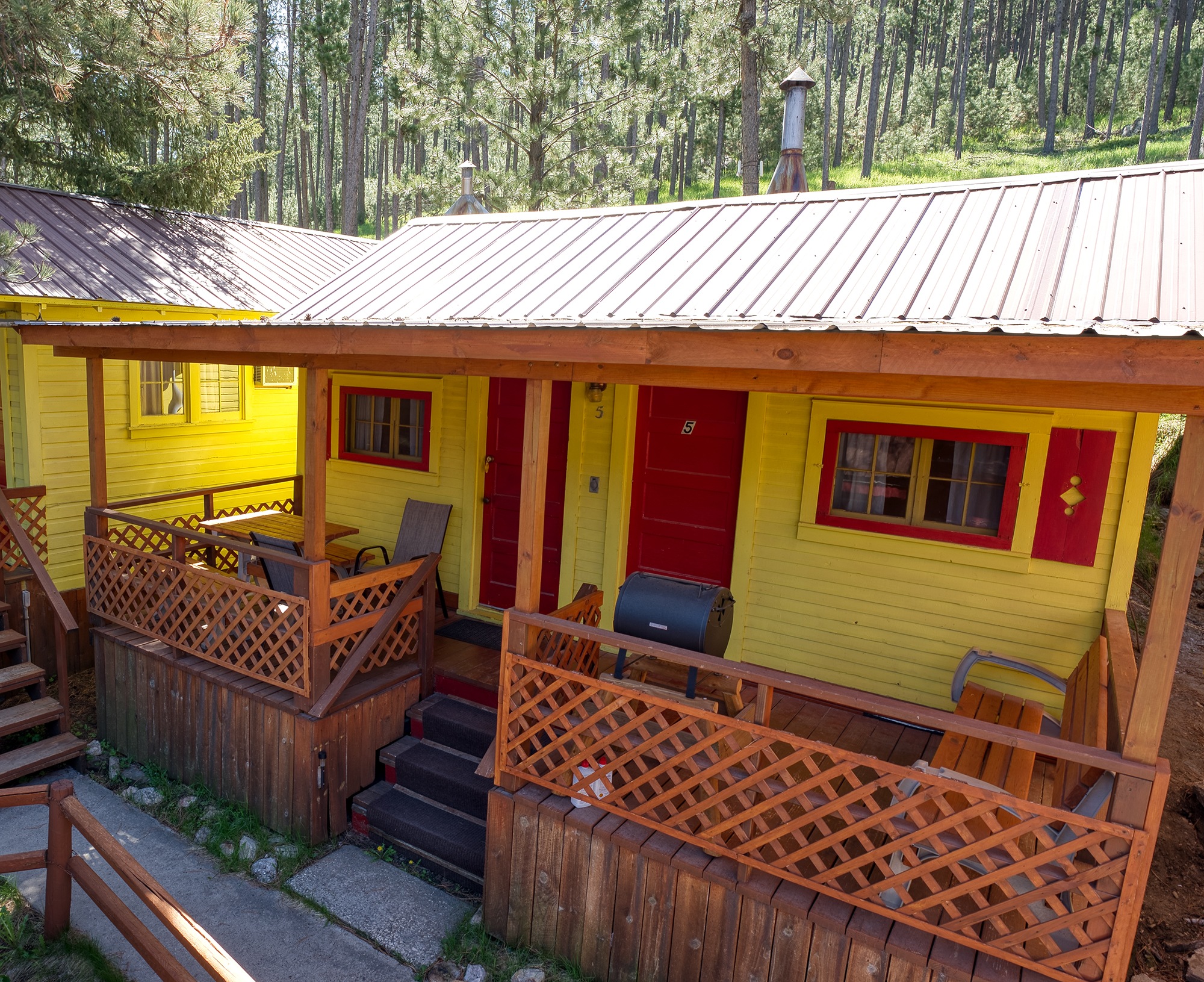 Cabin 5: yellow cabin with red doors, a charcoal grill, steps and a covered porch